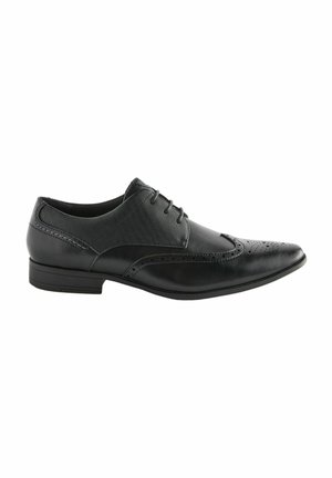 Zapato de vestido negro de cuero con parte superior de tela, punta afilada, detalles perforados y un tacón bajo y rectangular. Diseño con cordones. Acabado liso.