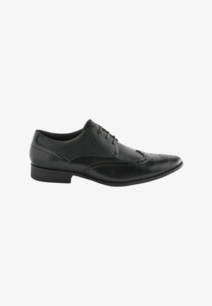 Black leather dress shoe with fabric upper, pointed toe, perforated detailing, and a low, rectangular heel. Laced design. Smooth finish.