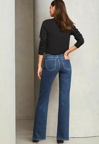 Temno modri razširjeni kavbojki z značilno denim teksturo, zasnovo s petimi žepe in diskretnimi šivi; kombinirani z črnim skrajšanim topom.