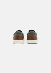 Lightweight sneakers with a grey textile upper, brown leather accents, white rubber sole, and navy lining. Features a minimalistic design.