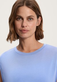 Světlomodrý top bez ruk ávů s kulatým výstřihem. Měkká, hladká látka s jemným leskem a detaily šití.