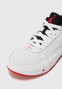 Valkoinen lenkkarit rei'itetyllä kuvioinnilla, mustilla nauhoilla ja punaisilla yksityiskohdilla. Sivussa ja pohjassa on "Jordan"-etiketti ja logo.