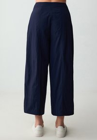 Marineblauwe wijde pants met een gladde textuur en een medium hoge tailleband, voorzien van verticale naden en een cropped lengte boven de enkels.
