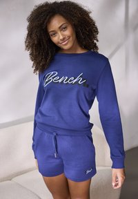 Blaues Sweatshirt- und Shorts-Set aus weichem Material, mit einem auffälligen "Bench."-Logo in kontrastierenden Farben. Lässiges Design mit Taschen.