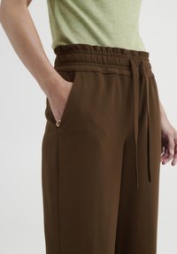 Braune, elastische Hosen mit Gummibund und Kordelzug sowie seitlichen Taschen. Aus glattem Material gefertigt, mit einem entspannten Schnitt und klaren Linien.