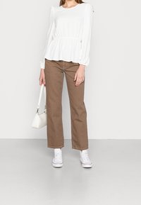 Maglietta peplum bianca a maniche lunghe, jeans dritti marroni, sneakers bianche e una piccola borsa bianca. Tessuto texturizzato e vestibilità rilassata.