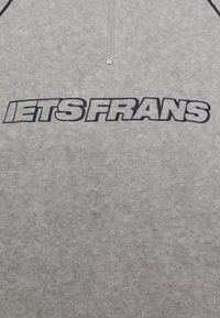 Grå fleece-tröja med en fjärdedels dragkedja, med tjock, broderad mörkblå text "IETS FRANS" tydligt visad på framsidan.