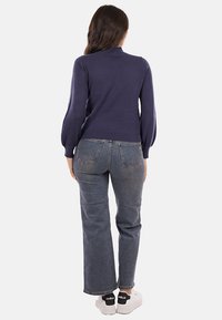Maglione blu navy con maniche a sbuffo, orlo a coste, abbinato a jeans in denim azzurro a vita alta e sneakers bianche con dettagli neri.