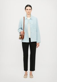 Light blue denim jacket with large front pockets, cream top, black trousers, and beige slip-on shoes; brown crossbody bag.