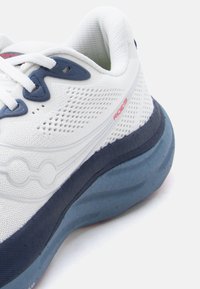 Άσπρο και ναυτικό παπούτσι για τρέξιμο με πλέγμα στο πάνω μέρος, χοντρή μπλε σόλα, άσπρα κορδόνια και κόκκινη σήμανση "Ride 19" στο πλάι.