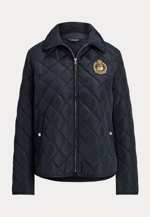 Laivastonsininen tikattu takki, jossa etuvetoketju, painonapilliset taskut, pystykaulus ja vasemmassa rinnassa kirjailtu vaakuna.