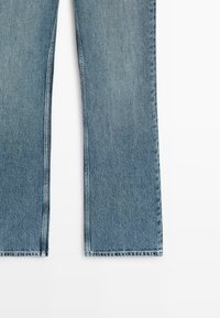 Blauwe denim jeans met rechte pijpen, zichtbare naden en een licht vervaagde textuur op een witte achtergrond.