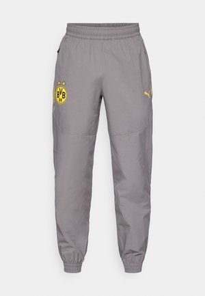 Grijze joggingbroeken met een elastische tailleband, ritssluiten zakken en een geel logo met sterren op het linkerbeen en het merlogo op het rechterbeen.