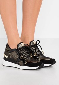 Czarno-złote buty sportowe wykonane z siateczki i zamszu, z wbudowanym obcasem, teksturowanymi akcentami i detalami sznurowadeł.