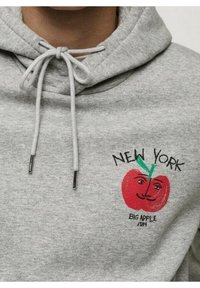 Grijze hoodie met een vooraanstaand grafisch ontwerp van een lachende appel met een groene steel, gelabeld "NEW YORK BIG APPLE 1894," en met een trekkoordsluiting.