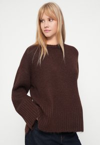 Καφέ πλεκτό πουλόβερ με χαλαρή εφαρμογή, ριγωτούς μανίκια και στρίφωμα. Μαλακή υφή με ελαφρώς πιο φαρδείς μανίκια.