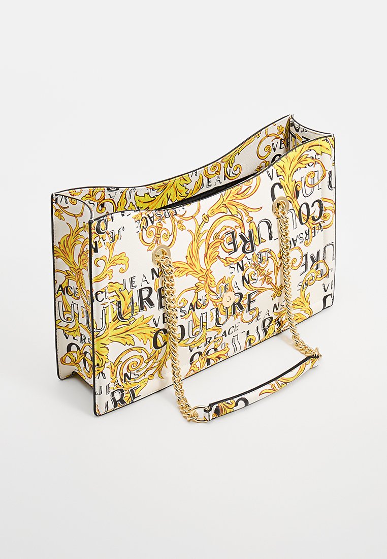 Weiße Tragetasche mit auffälligen schwarzen und gelben Buchstaben, kunstvollen goldenen Blumenmustern und einem goldenen Kettenriemen.