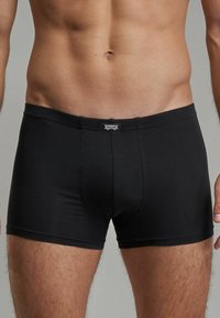 Black cotton boxer shorts with a comfortable waistband, featuring a label on the front and a snug fit around the thighs.