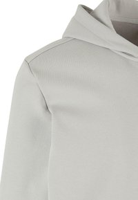 Sweat à capuche gris clair avec vue rapprochée du haut de la poitrine, de la couture de l'épaule et de la capuche attachée.