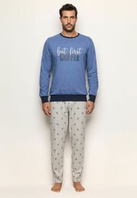 Camicia a maniche lunghe blu con grafica "ma prima caffè", abbinata a pantaloni da pigiama grigi con motivo a tazza di caffè. Tessuto morbido, vestibilità rilassata.