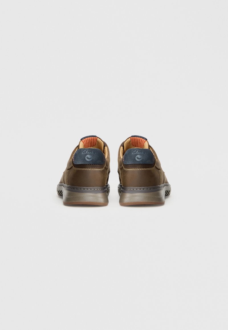 Zapatos de cuero marrón con forma redondeada, con un acento en el tacón en color marino y forro de tela naranja. Suela de goma texturizada para mayor agarre.