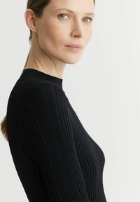 Czarny sweter o prążkowanej strukturze, z wysokim dekoltem i dopasowanym krojem, eksponujący pionowe linie i miękką teksturę.