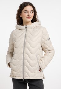 Beige gewatteerde pufferjas met een capuchon, met een golfpatroon, ritssluiting aan de voorkant en zijzakken. De stof is glad met een subtiele glans.