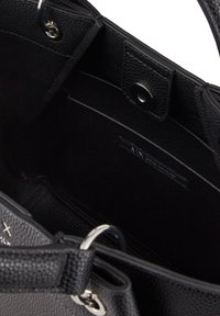 Interno di una borsa a spalla nera in pelle con finitura tessurizzata, dotata di chiusura con calamita, hardware in argento e un'etichetta interna.