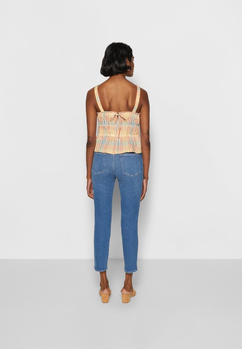 Rutig crop topp i pastellfärger med smockad baksida, justerbara axelremmar, i kombination med åtsittande blå jeans och ljusa träklackar.