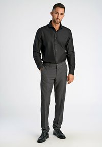 Zwarte button-up shirt met een soepele textuur, gecombineerd met grijze broek met een subtiel patroon en zwarte leren schoenen.