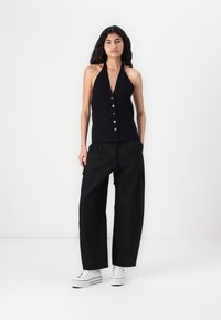 Zwarte haltertop met geribbelde textuur en knopen aan de voorkant, gecombineerd met losse zwarte broek en witte sneakers. Eenvoudig ontwerp en monochrome kleuren.