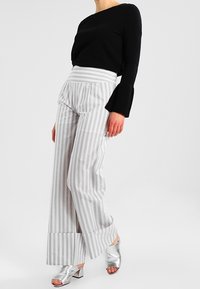 Raitahousut leveillä lahkeilla, vaaleanharmaata ja valkoista, joissa on korkeavyötärö ja kellotettu lahkeen suu. Yhdistetty mustaan pitkähihaiseen toppiin ja hopeisiin korkokenkiin.