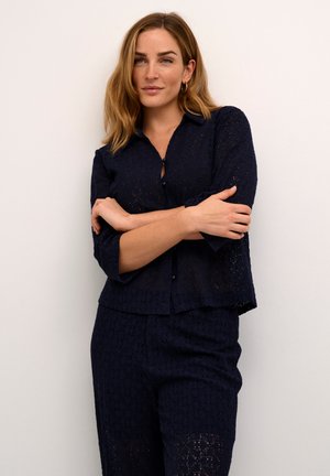 Camicia in pizzo blu navy con chiusura a bottoni sul davanti, vestibilità comoda, maniche a tre quarti e orlo a strati, abbinata a pantaloni in pizzo coordinati.
