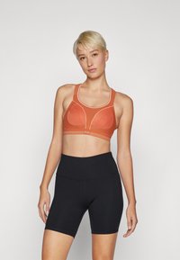 Orange sport-BH med ribbet tekstur, buede sømmer og kontrasterende hvite detaljer. Kombinert med sorte høytaljede shorts.