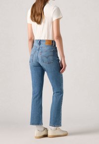 Jean en denim bleu à taille haute avec une jambe fuselée et un léger effet délavé. Présente une étiquette en cuir marron sur la ceinture arrière et des poches arrière classiques.