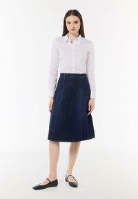 Marineblaue A-Linien-Rock in knielanger Länge, mit taillierter Passform und minimalistischen Nähdetails. Kombiniert mit einer weißen Hemdbluse.