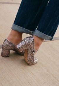Scarpe con tacco a blocco glitterate e multicolori, con punta rotonda e cinturino, indossate con jeans in denim blu scuro risvoltati.