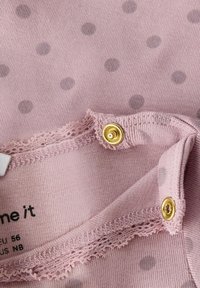 Różowy materiał z małymi szarymi kropkami, zdobione koronkowym wykończeniem i dwoma złotymi zatrzaskami na krawędzi.