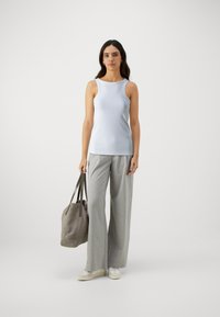 Débardeur à côtes bleu clair associé à un pantalon large à carreaux gris. Le modèle tient un sac fourre-tout gris et porte des baskets blanches.