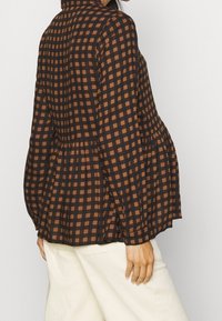 Blouse à carreaux marron et bleu marine avec un design péplum, manches longues et col à revers. Fabriquée en tissu léger.