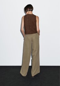 Top en suedine sans manches marron associé à un pantalon large kaki, présentant un design épuré et une texture lisse, sur un fond uni.
