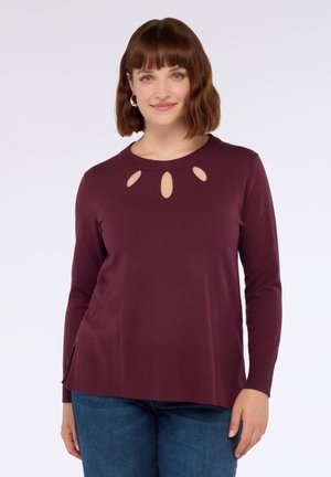 Il maglione lungo a maniche con taglio maroon presenta dettagli scavati intorno al colletto, orlo a coste e spacco laterale per facilitare il movimento. Tessuto morbido e testurizzato.