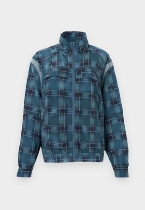 Blå og svart rutete jakke med glidelås, høy krage, lange ermer, elastisk kant og reflekterende lapper på overarmene.