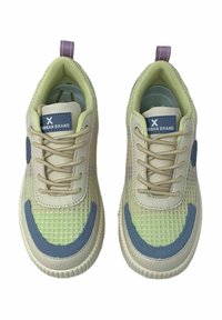 Zapatillas deportivas con un cuerpo de malla beige claro y detalles en verde, presentando parches laterales azules, cordones redondos y una pestaña de talón púrpura.