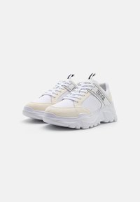 Sneakers realizzati in tessuto bianco e suede crema, dotati di una suola spessa, design con lacci e marchio sul lato e sulla linguetta.