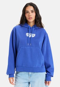 Sudadera azul hecha de una tela suave, con un bolsillo tipo canguro, puños acanalados y cordones. Tiene un logo impreso en blanco en la parte frontal.