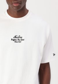 White cotton t-shirt featuring black embroidered logo "New Era" with "Buffalo, New York Since 1920" on the front. Short sleeves, crew neck.