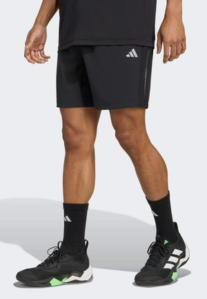 Shorts de sport noirs avec le logo Adidas gris, associés à des chaussettes et des chaussures noires avec des accents verts et des rayures blanches.