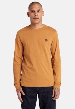 Long-sleeve, mustard-colored t-shirt made of cotton, featuring a small, dark logo on the left chest. Plain design with crew neck.