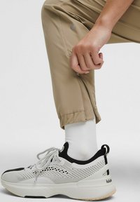 Sportieve schoen met een bovenwerk van mesh in wit en zwart, met een gestructureerde zool. Gepaard met beige tapered joggers en een witte sok.